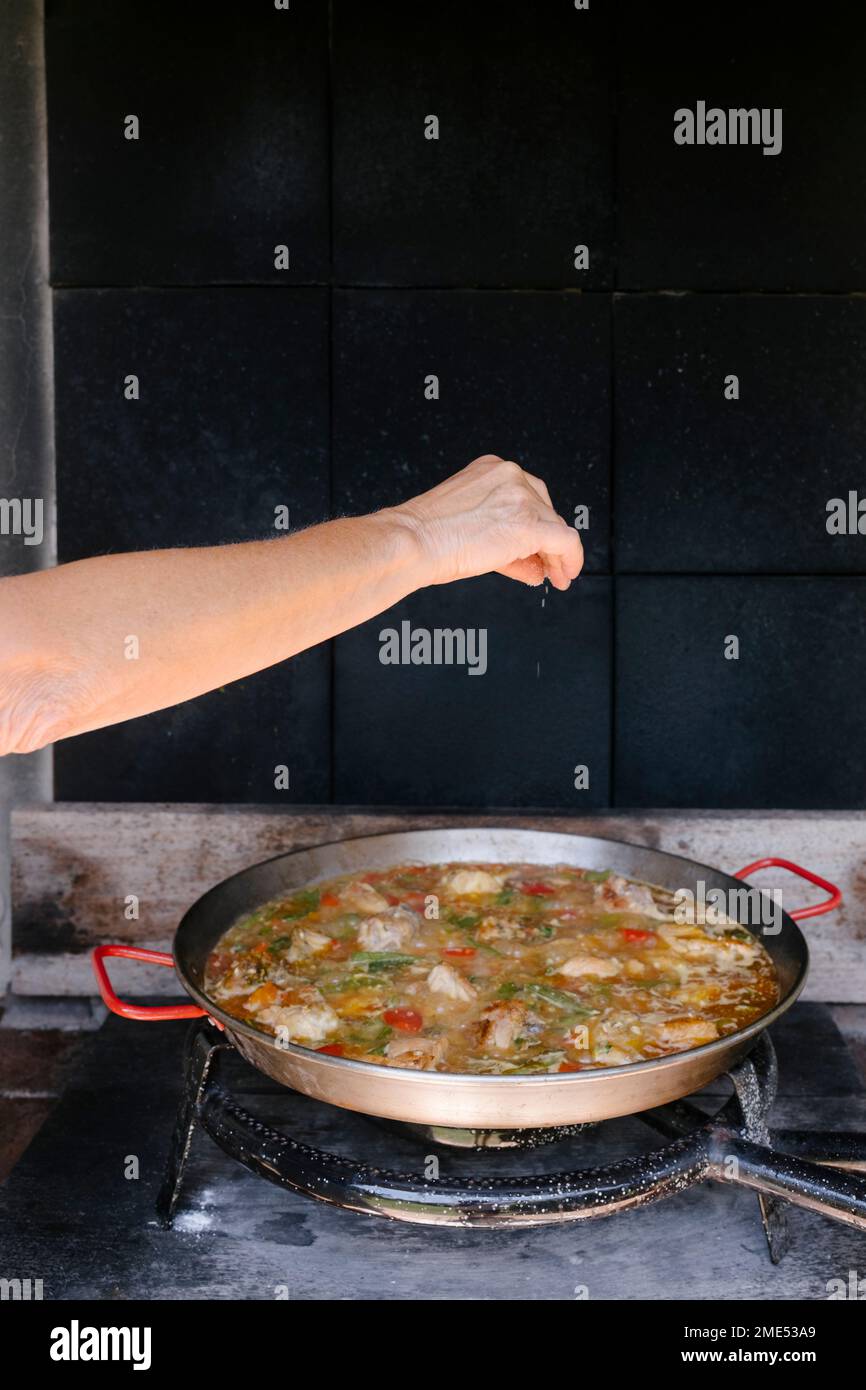 Donna spruzzare condimenti sulla paella in cucina all'aperto Foto Stock
