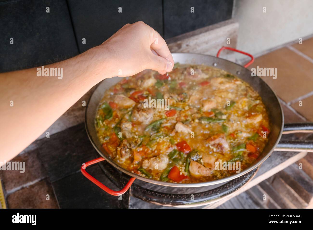 Mano dell'uomo che aggiunge la paella preparante alla cucina esterna Foto Stock