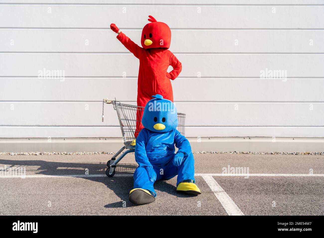 Donna che indossa costume rosso in piedi nel carrello della spesa con l'uomo seduto a terra Foto Stock