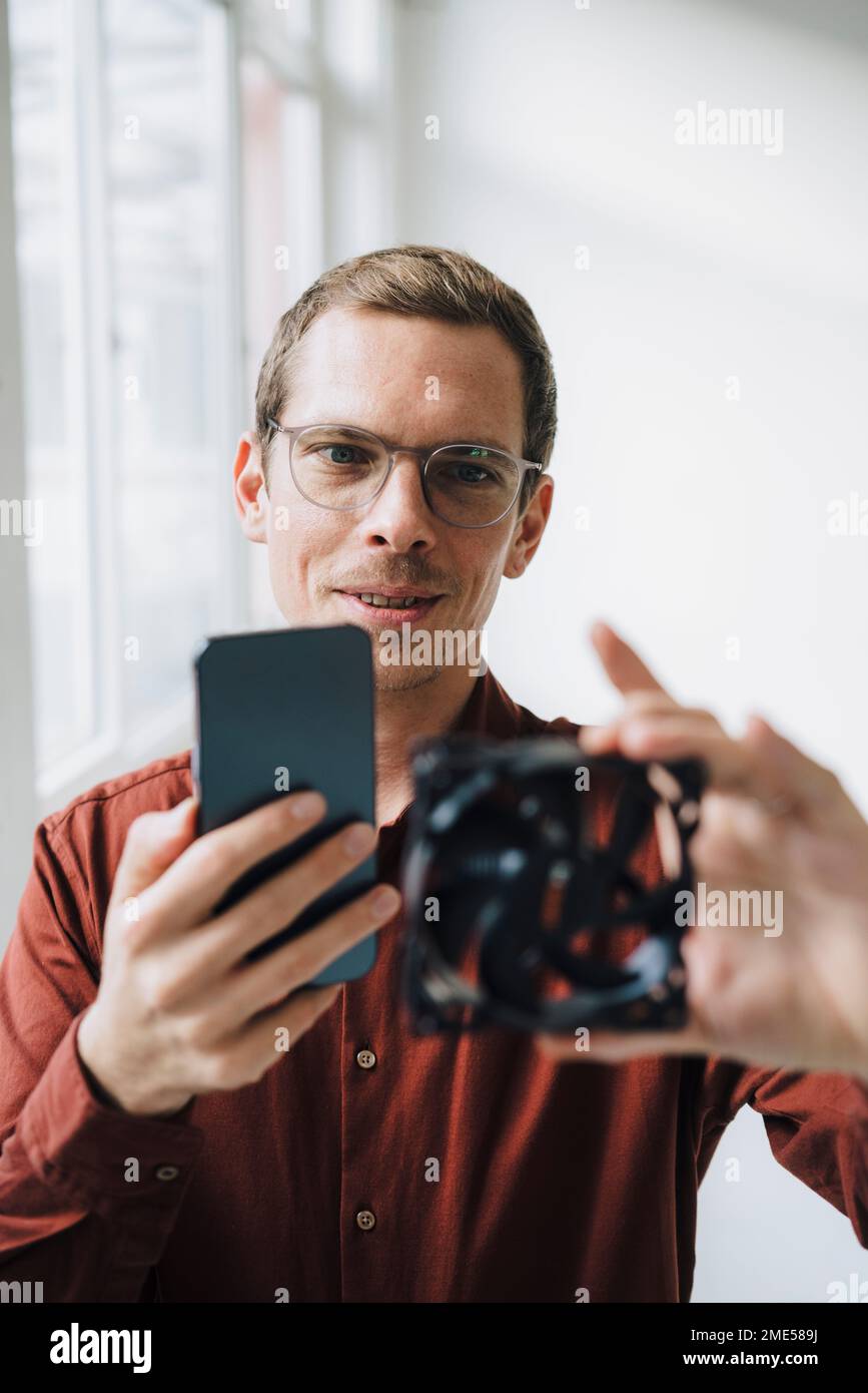 Uomo d'affari che fotografa il ventilatore elettrico attraverso lo smartphone Foto Stock