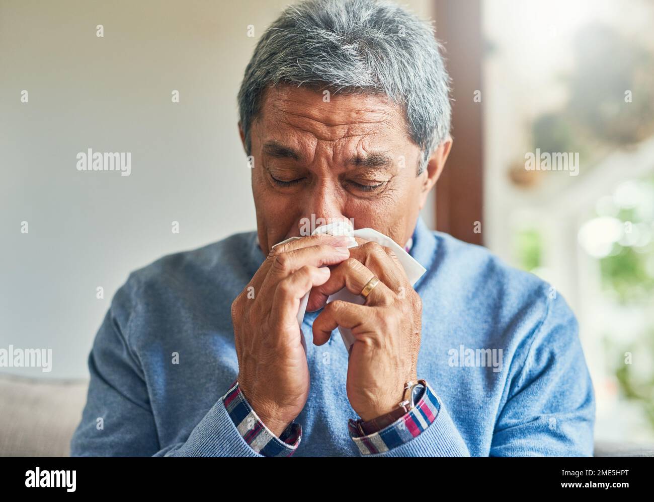Le allergie sono le peggiori. un uomo anziano falce che soffia il naso con un tessuto a casa. Foto Stock