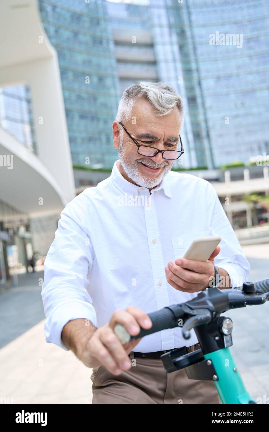 Felice uomo anziano che utilizza l'app mobile per il noleggio di biciclette nel parco cittadino. Foto Stock