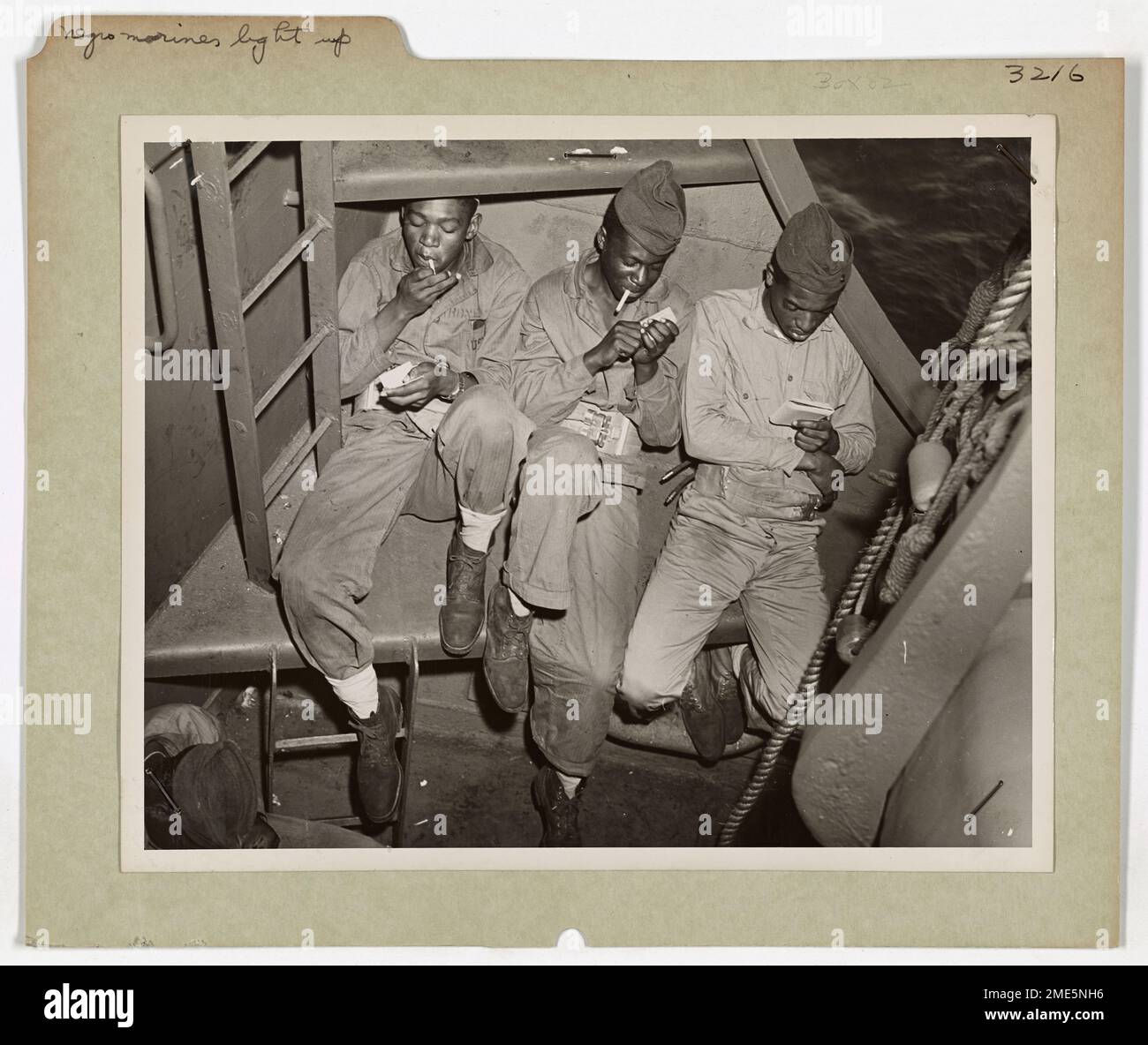 Questa fotografia mostra tre marine afroamericani che si rilassano a bordo di una nave da trasporto con equipaggio della Guardia Costiera diretta verso le aree di invasione del Pacifico. L'immagine cattura un momento tranquillo prima dell'intensità della battaglia. Foto Stock