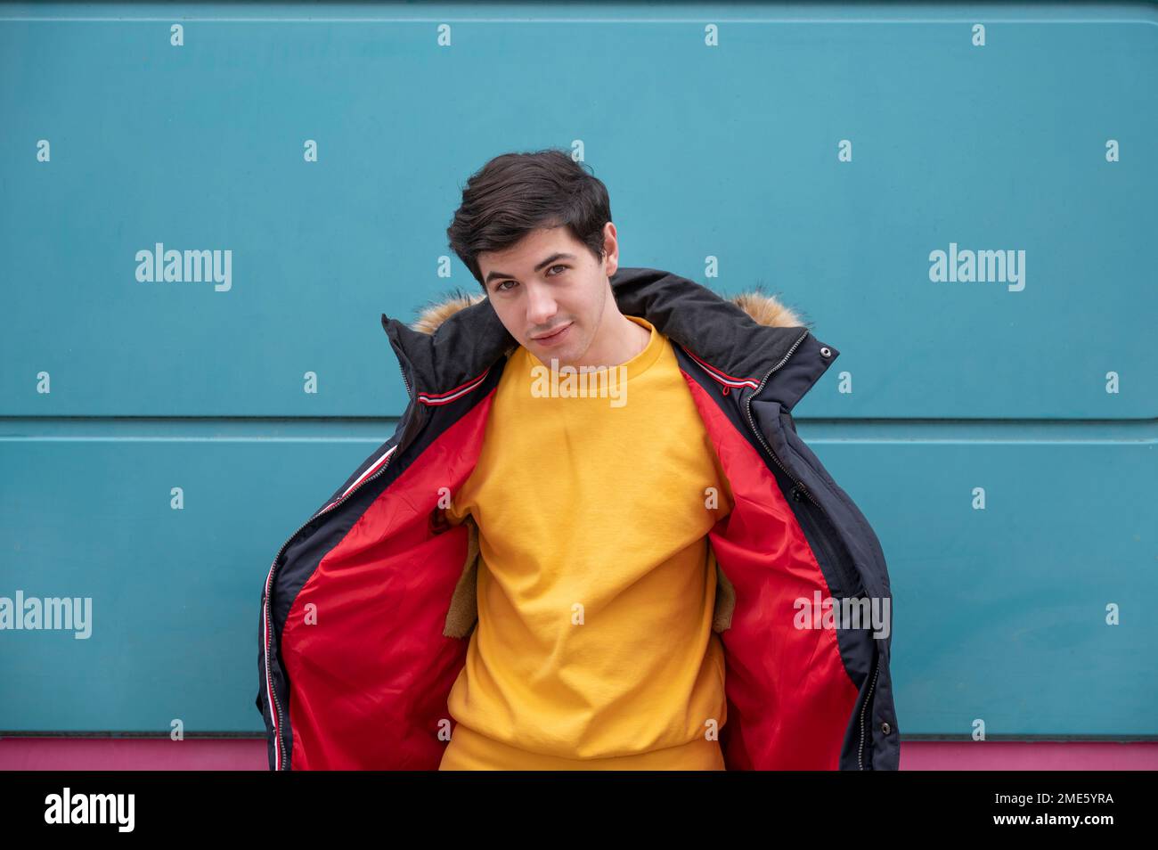 Un giovane uomo in un maglione giallo e una giacca rossa su sfondo blu. Foto Stock
