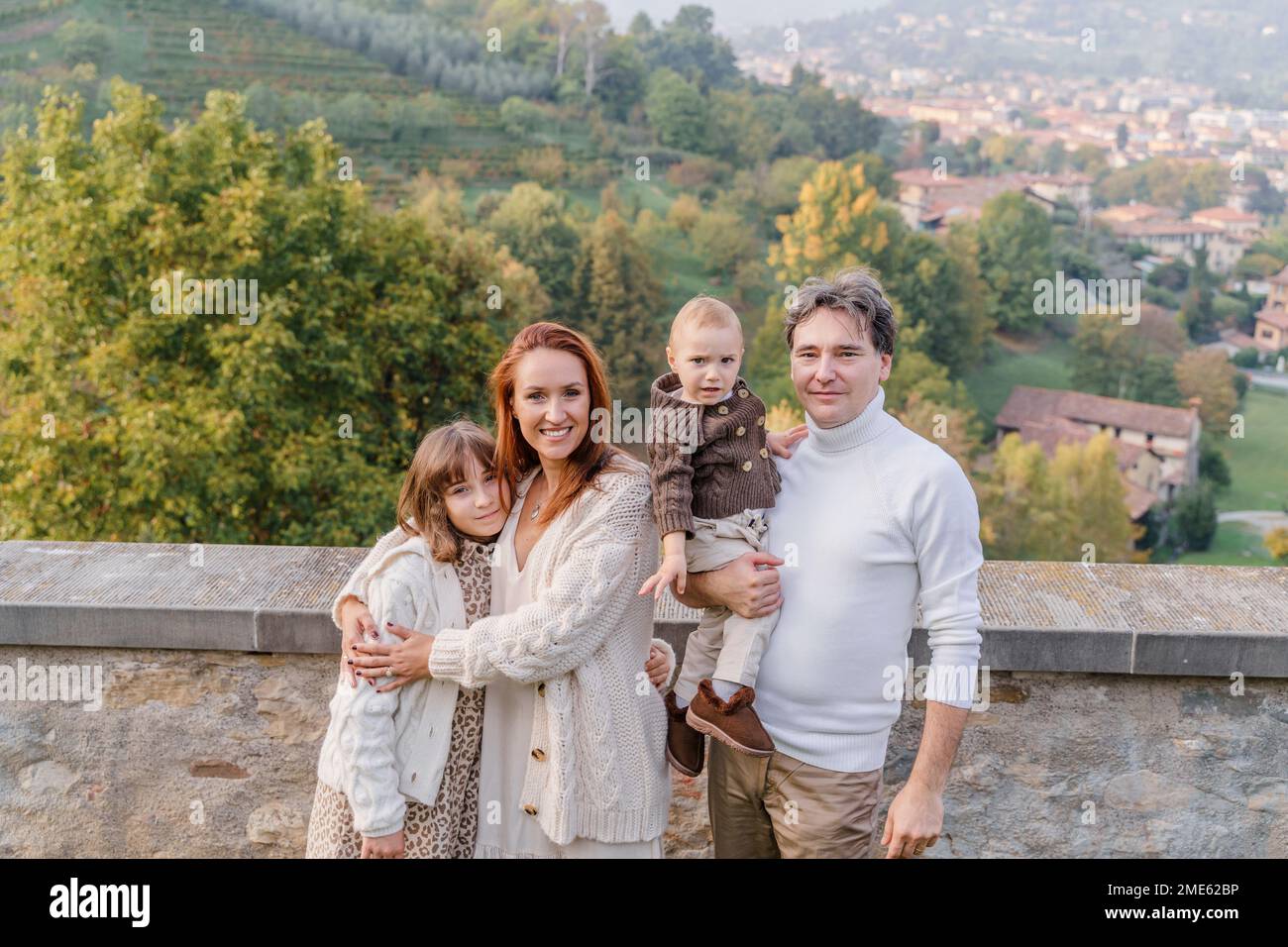 Una giovane famiglia con due figli, una adolescente e un bambino, si trova sullo sfondo delle verdi colline e dei vigneti italiani della città Foto Stock