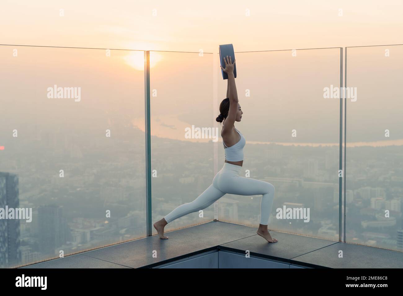 Ritratto di giovane bella donna asiatica che pratica un esercizio di yoga sui tetti durante il tramonto. Calma e relax, felicità femminile. Immagine orizzontale Foto Stock