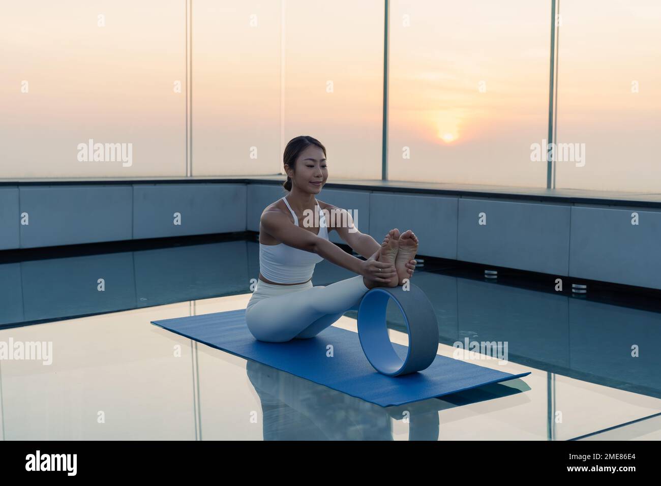 Ritratto di giovane bella donna asiatica che pratica un esercizio di yoga sui tetti durante il tramonto. Calma e relax, felicità femminile. Immagine orizzontale Foto Stock