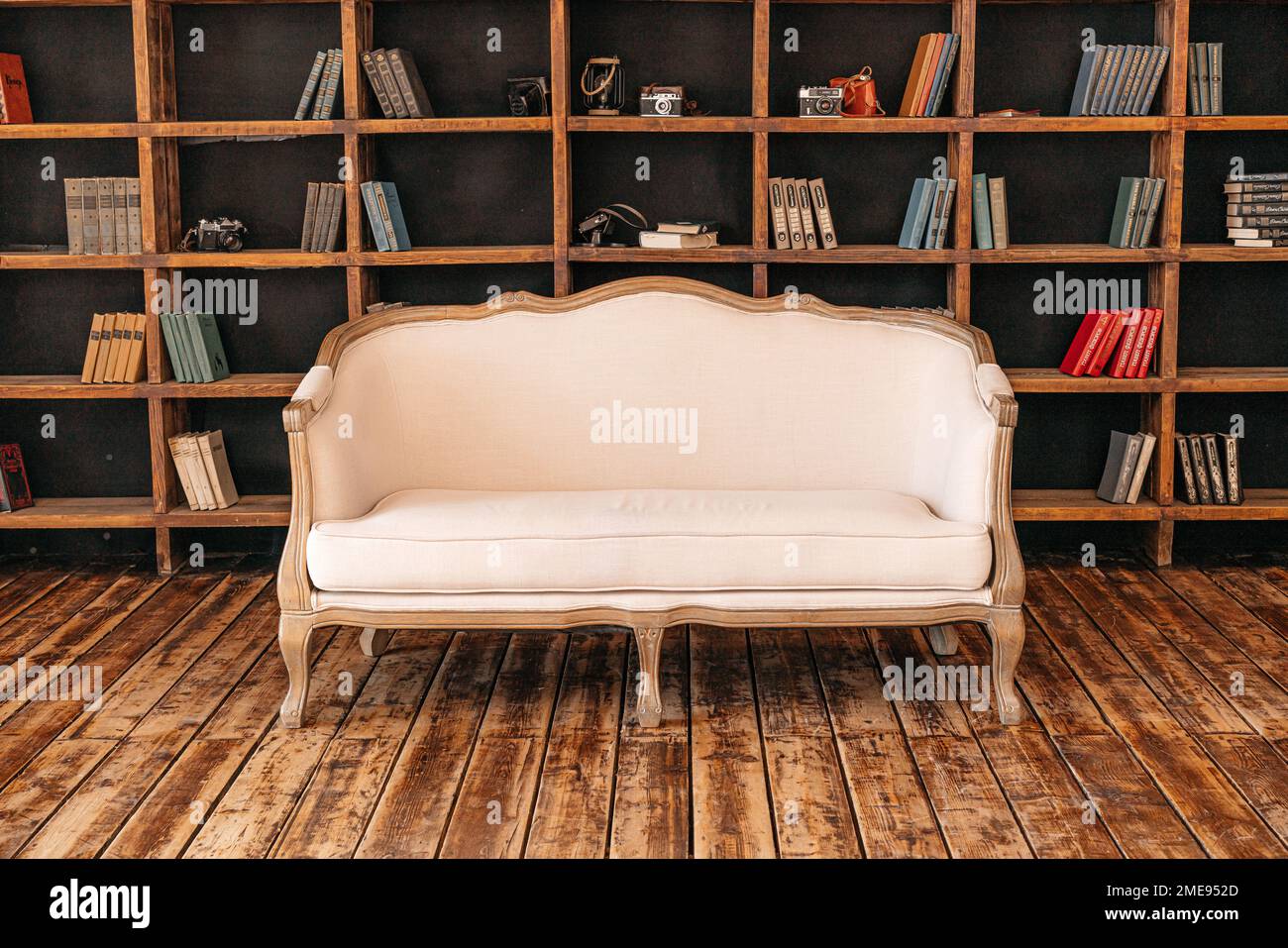 Divano retrò bianco in piedi nel soggiorno con un elegante design d'interni e collezioni di libri sulle librerie della biblioteca. Studio. Foto Stock