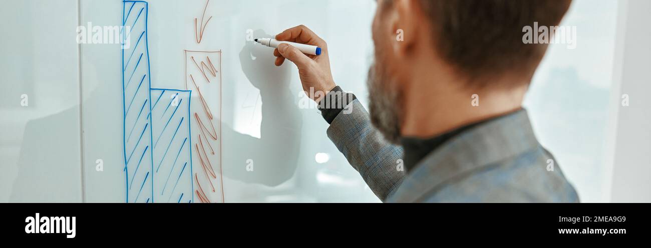 Uomo d'affari adulto in piedi e scrivere su lavagna bianca in ufficio Foto Stock