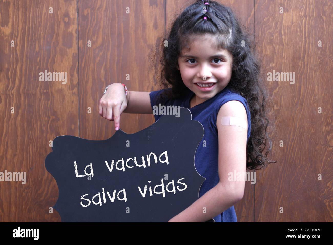 Bambina latina con capelli ricci mostra il suo braccio recentemente vaccinato contro il Covid-19 con un segno nero che dice 'il vaccino salva vite' Foto Stock
