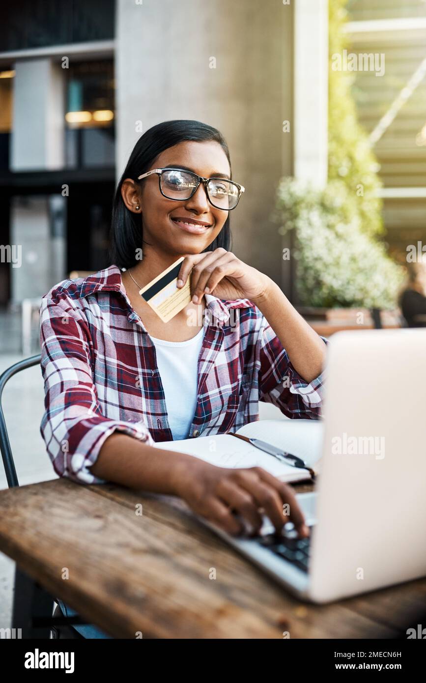 Risparmio per il mio futuro dopo l'università. una giovane studentessa che utilizza un computer portatile e una carta di credito all'esterno del campus. Foto Stock