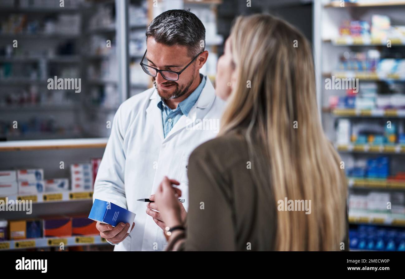 Permettetemi di scrivere le istruzioni qui. un farmacista maturo che assiste una giovane donna in un chimico. Foto Stock