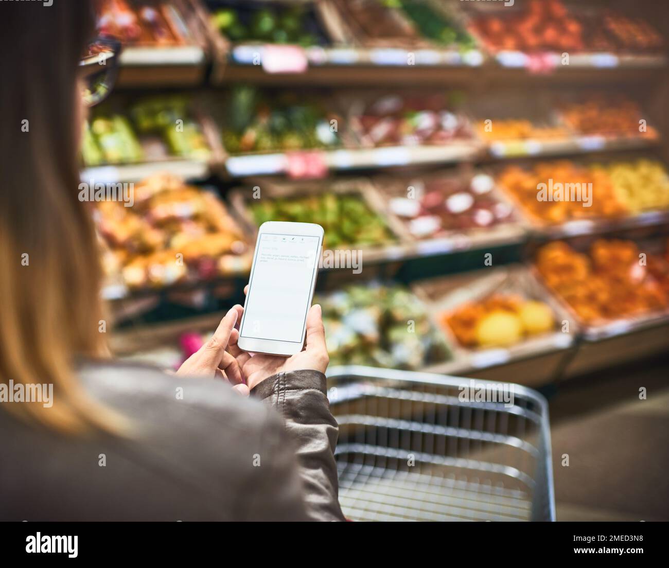 Risparmiate carta, utilizzate un'app per la lista della spesa. una donna che utilizza un telefono cellulare in un negozio di alimentari. Foto Stock