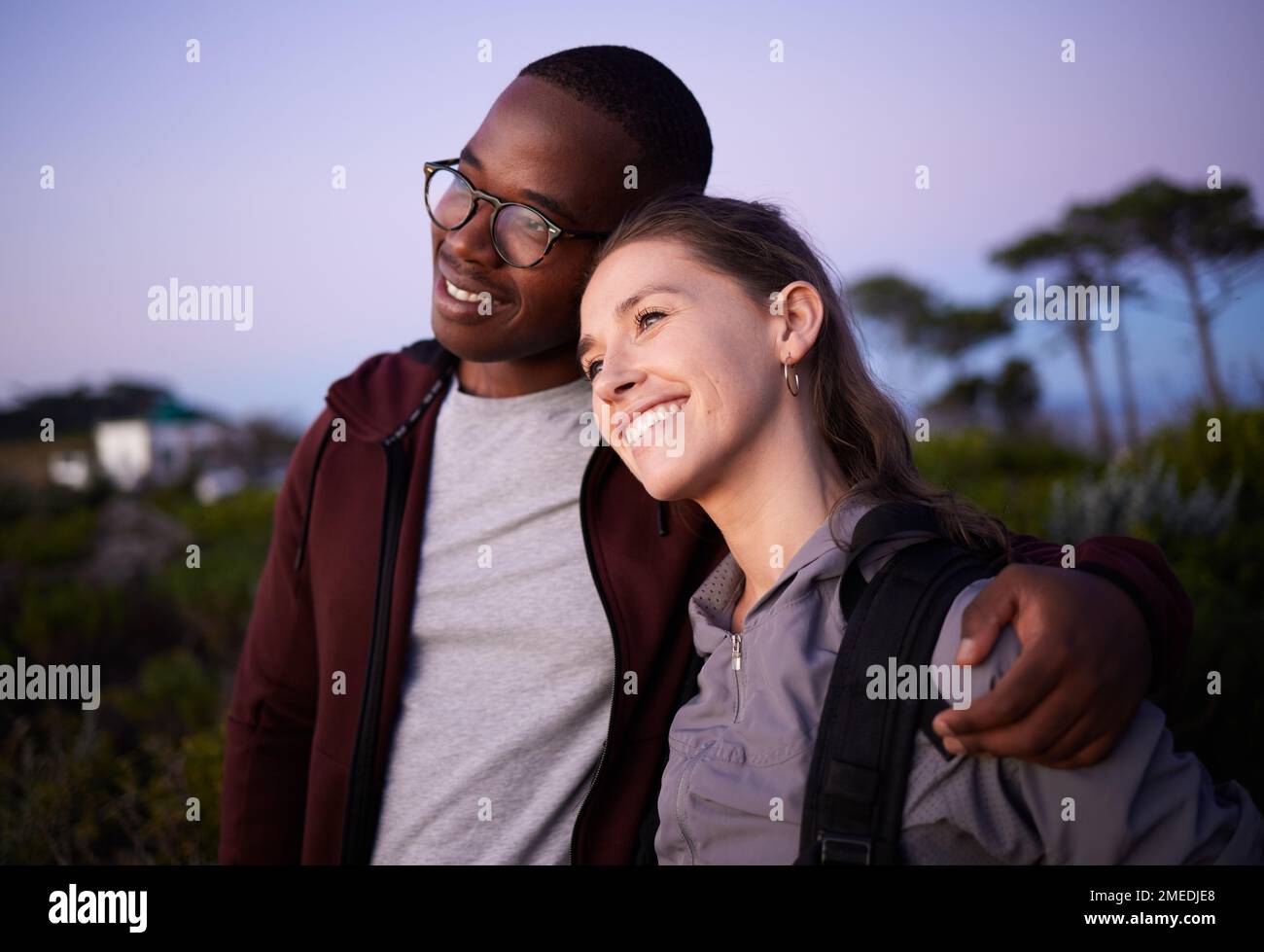 Coppia felice, relax e amore in un rapporto interracial durante il tramonto di sera o di notte all'aperto in natura. Avventura, viaggi e persone Foto Stock