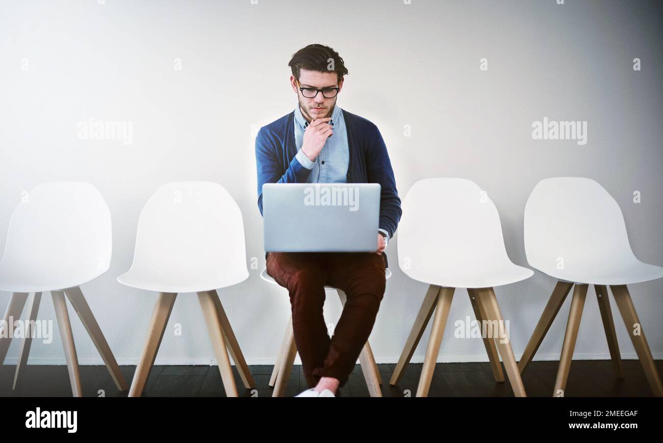 Fare un quiz online per aiutare con la sua intervista. un giovane uomo d'affari che usa un computer portatile mentre aspetta in coda. Foto Stock