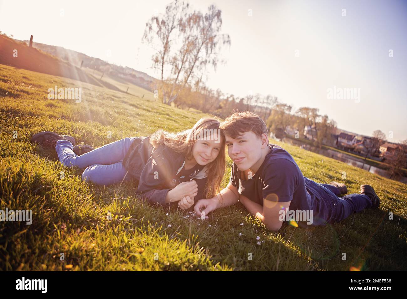 Fratello e sorella, fratelli, ragazzo e ragazza, bambini al tramonto, su un prato, erba, osservando i fiori e la natura. Condividere, piacevole momento in famiglia Foto Stock