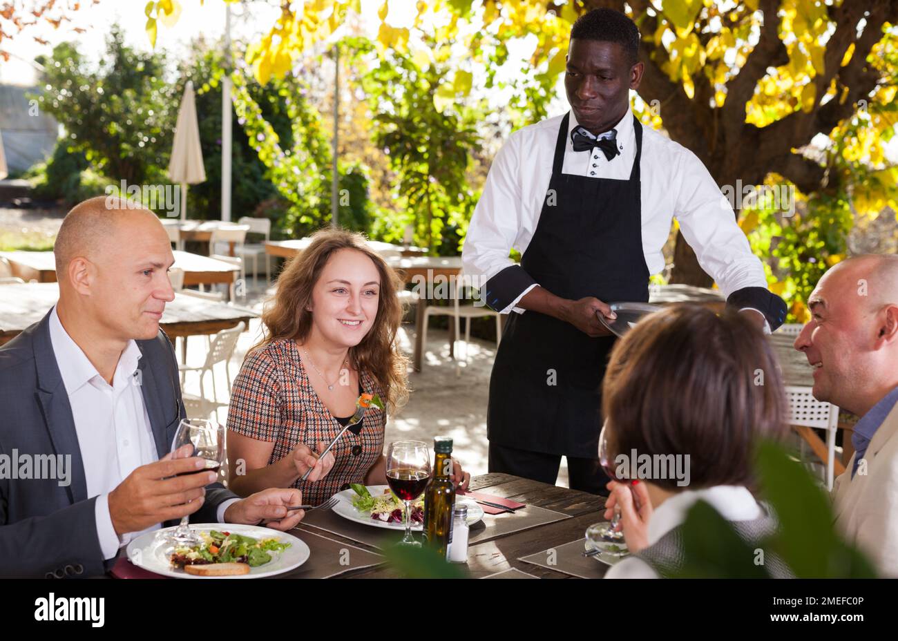 Cameriere che serve pasti al cordiale compagnia presso il ristorante all'aperto Foto Stock