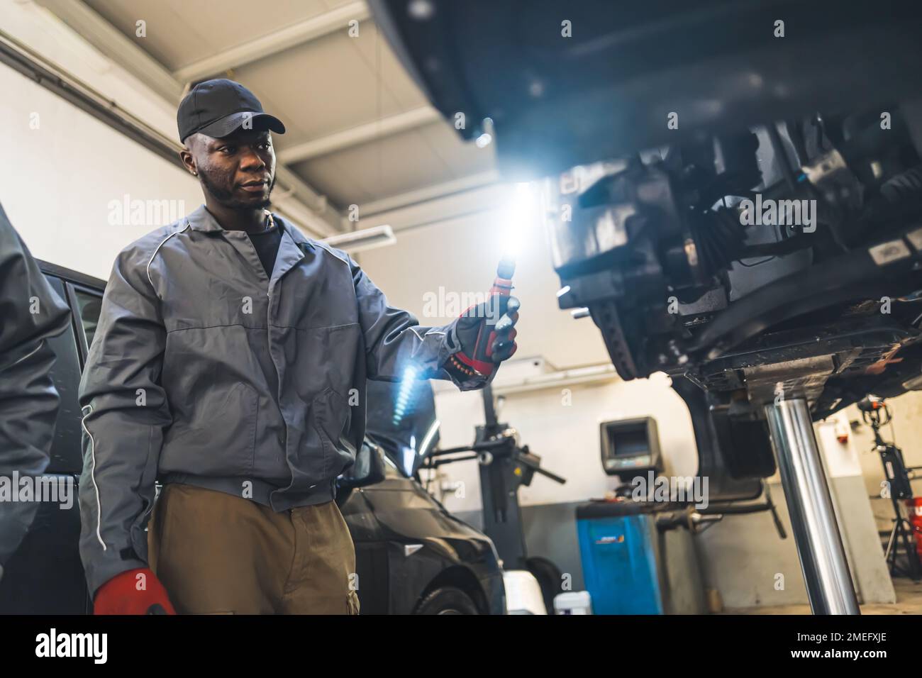 Inquadratura ad angolo medio-basso di un meccanico che controlla un'auto con una luce. Concetto di officina di riparazione. Foto di alta qualità Foto Stock