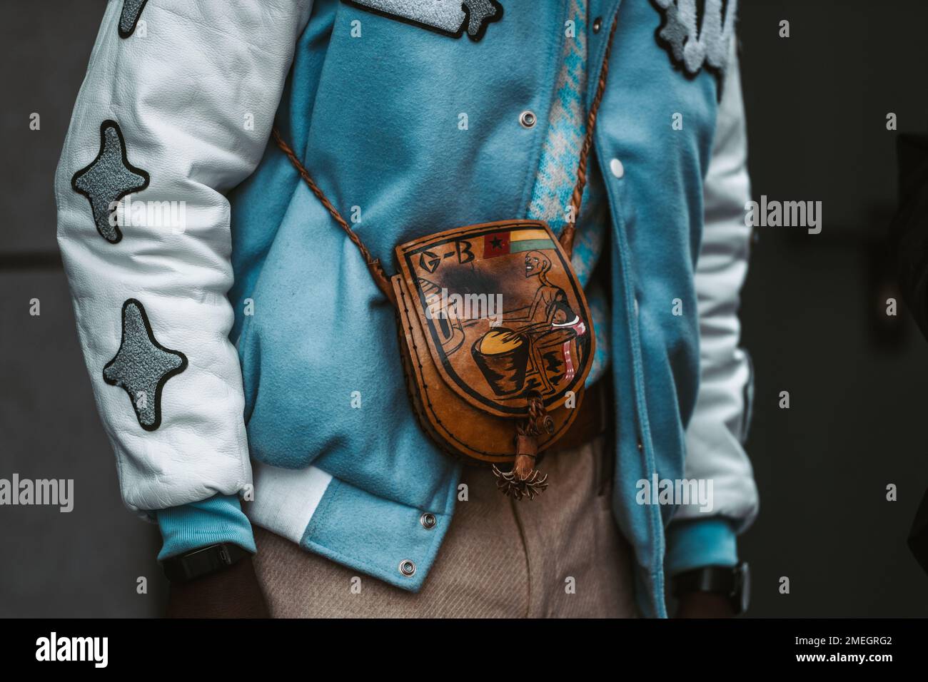 Milano, Italia - 24 febbraio 2022: Persona anonima in giacca bomber blu con maniche bianche e borsa in pelle marrone stampata. Foto Stock