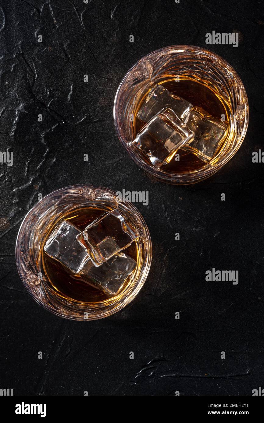 Whisky in bicchieri con ghiaccio. Whisky al bourbon sulle rocce su fondo di ardesia nera, girato dall'alto Foto Stock