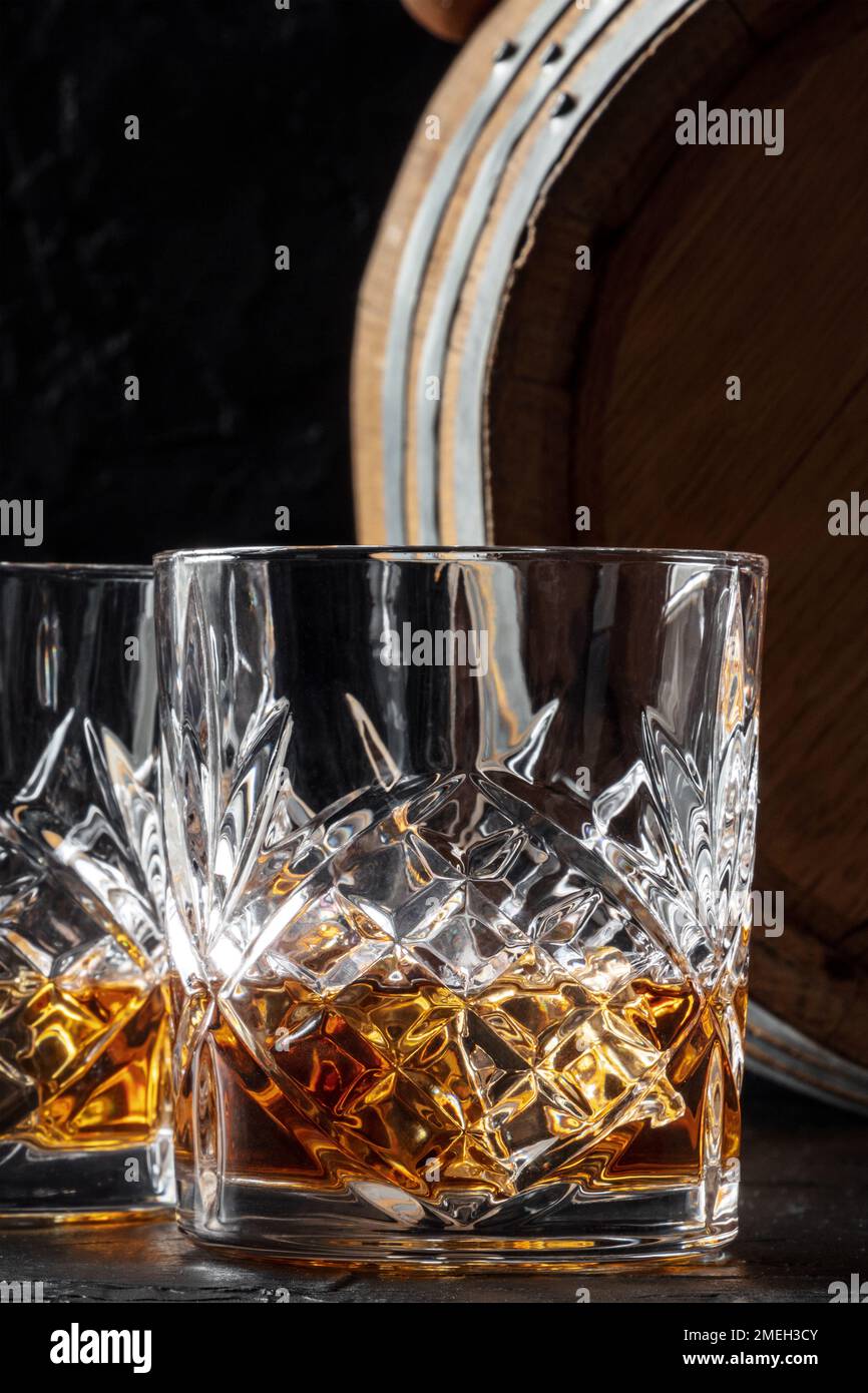 Frullare in un bicchiere con un barile. Whisky Bourbon e una botte su sfondo scuro, un elegante primo piano Foto Stock