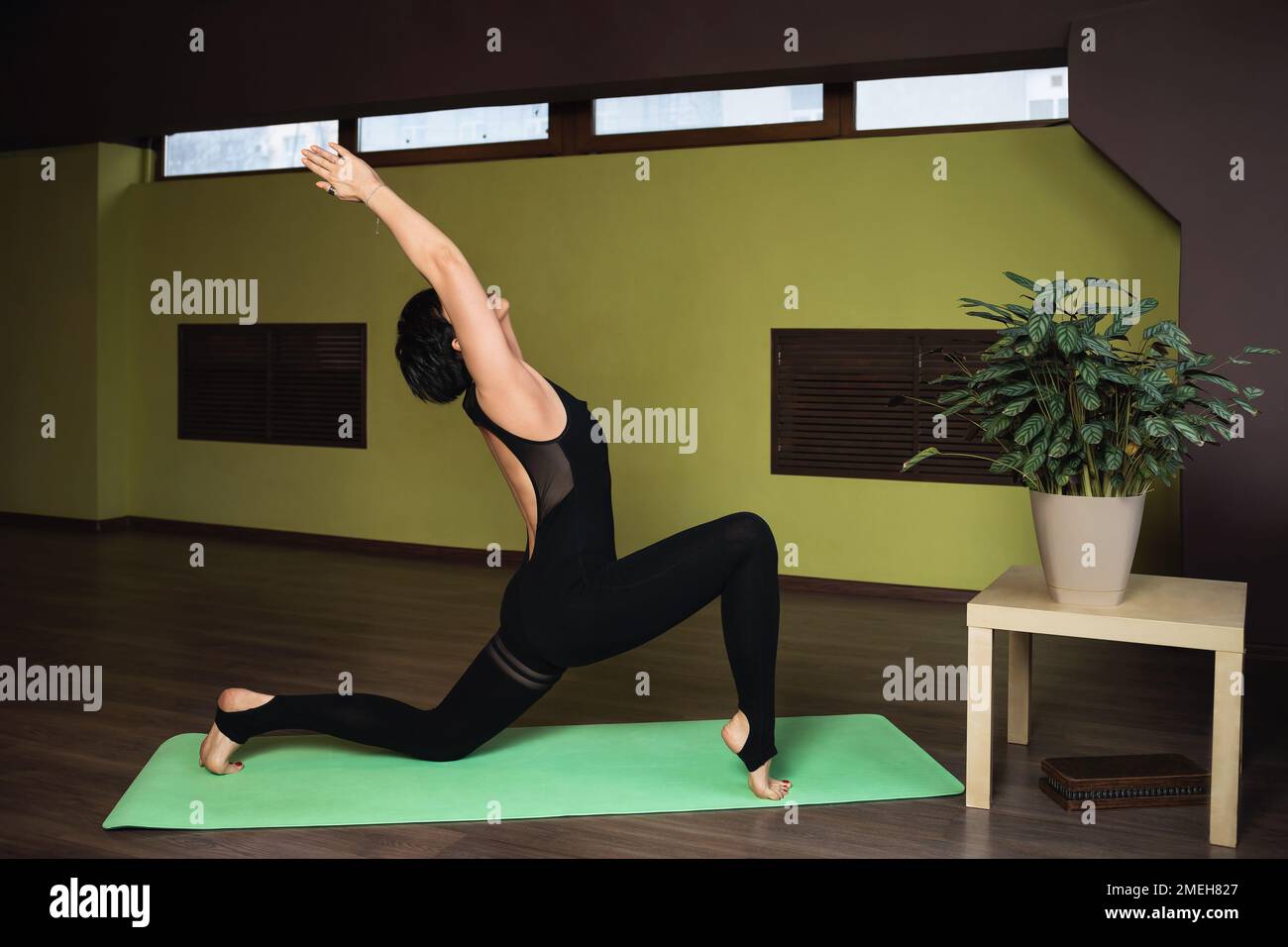 Attraente donna di mezza età, che conduce uno stile di vita sano e pratica yoga, esegue l'esercizio Anjaneyasana, una posa crescente, si allena da sola nella st Foto Stock