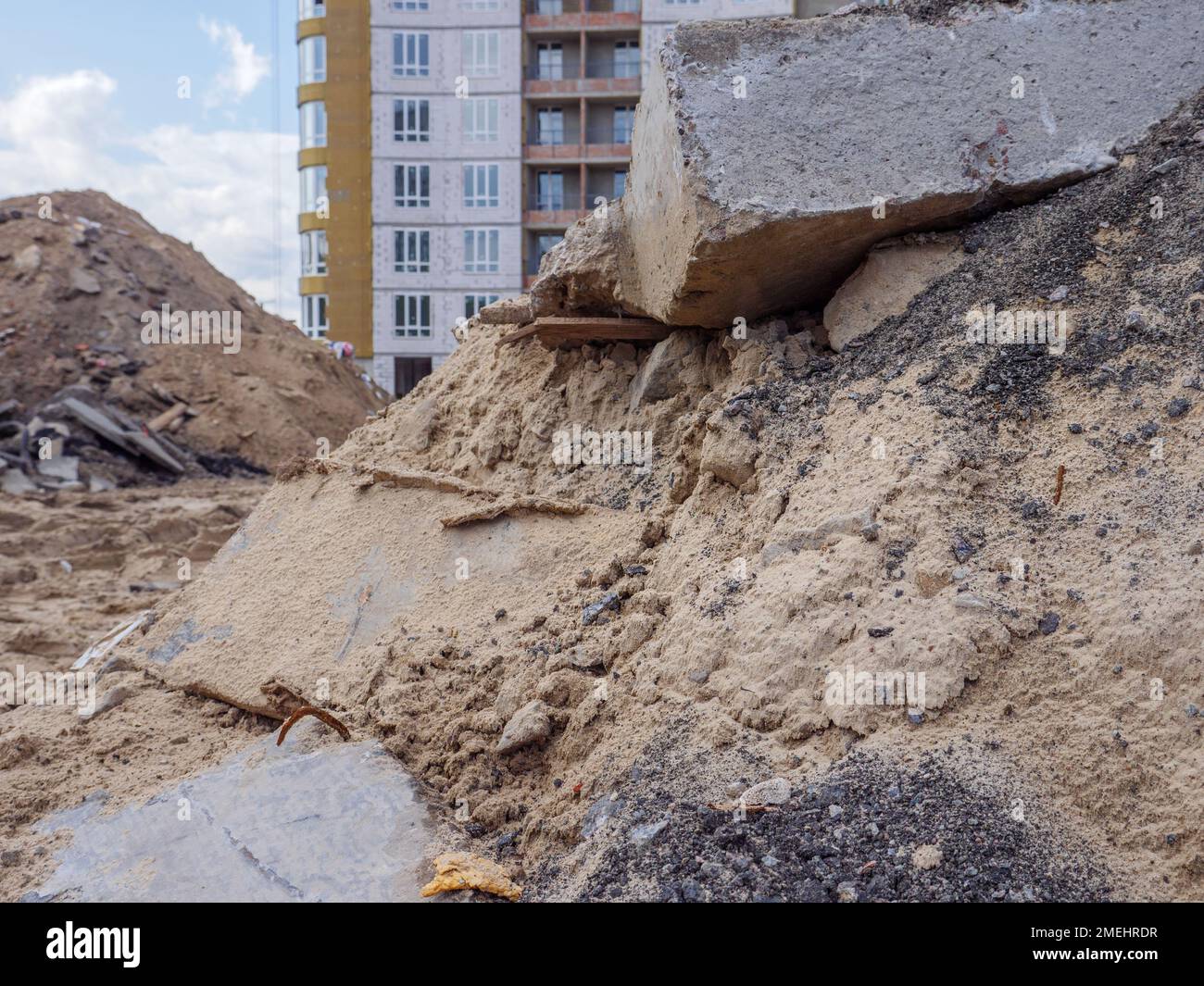 Un edificio con mucchi di sabbia e un enorme blocco di cemento in primo piano e un nuovo alto edificio sullo sfondo a Kyiv. Nuovo concetto di distretto. Foto Stock