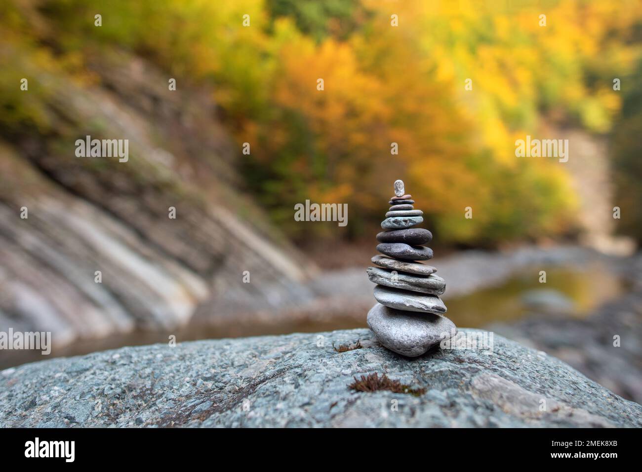 Stack di pietra con pietre equilibrate su sfondo di montagna sfocato al tramonto luce calda nel fogliame autunnale Foto Stock