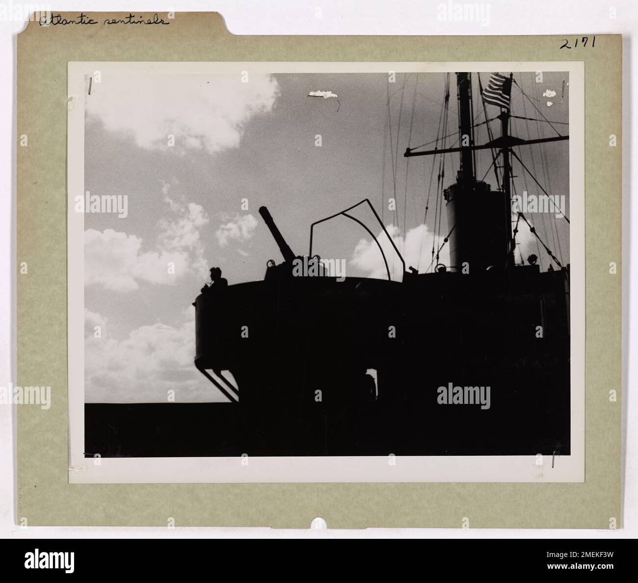 Una guardia costiera solitaria sul ponte di un cutter da combattimento scansiona il cielo alla ricerca di aerei nemici, con una pistola pronta all'azione. Il cutter è di stanza nell'Atlantico, a guardia contro potenziali minacce degli aerei dell'asse. Foto Stock