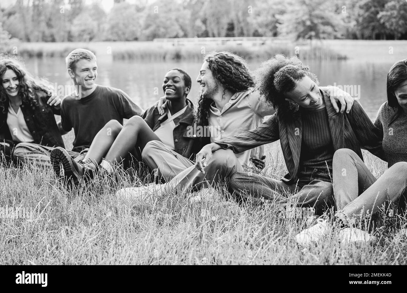 Amici multietnici che si divertono seduti sull'erba all'aperto - Focus sulla faccia destra della ragazza africana - montaggio in bianco e nero Foto Stock