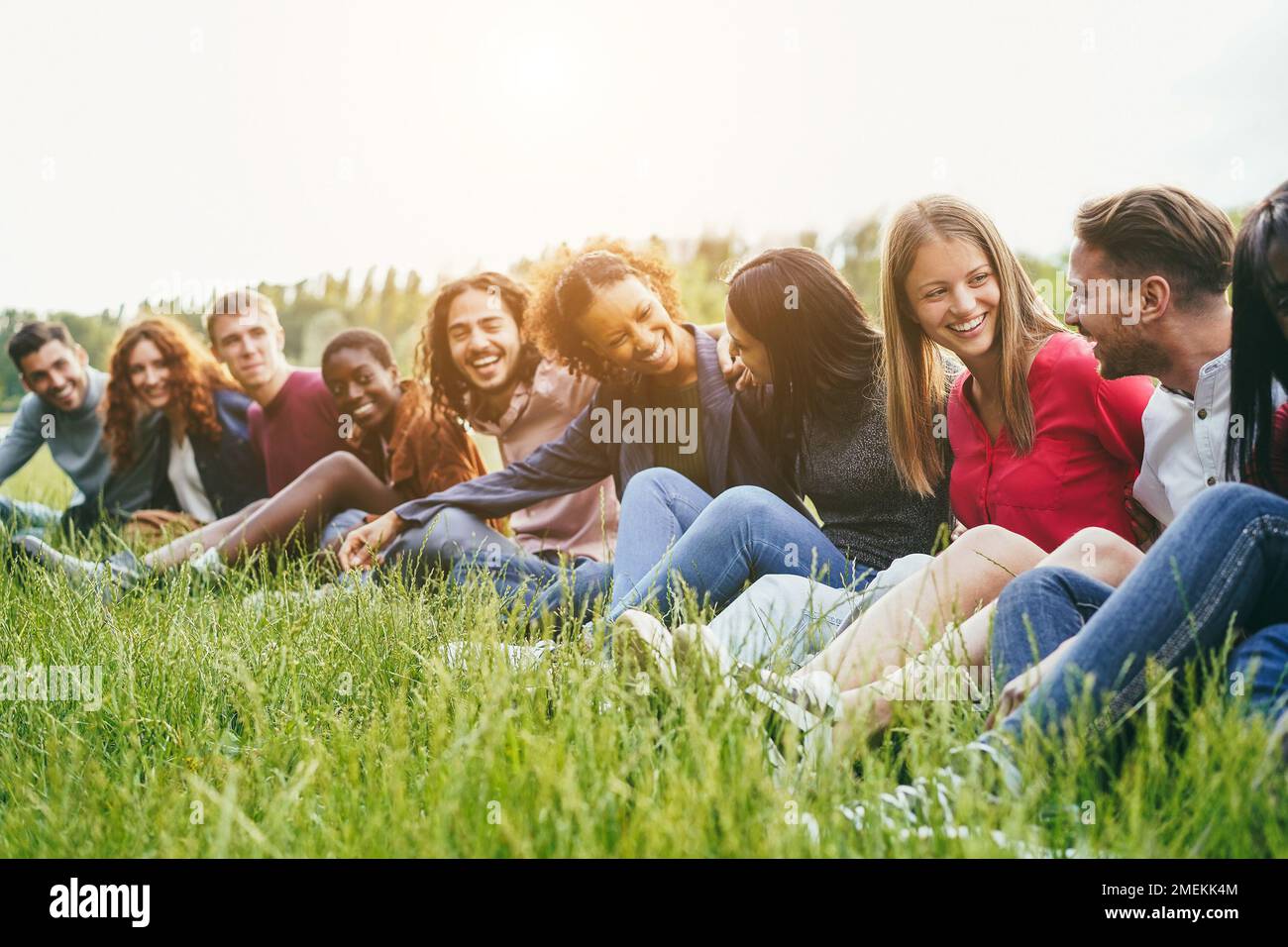 Amici multietnici che si divertono seduti sull'erba all'aperto - Focus sul volto della ragazza destra Foto Stock