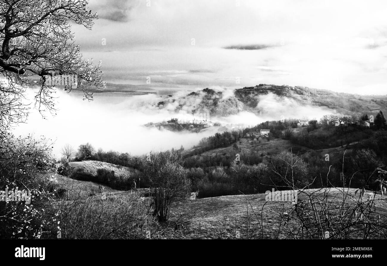 Paesaggio di borgo collinare avvolto nella nebbia, Appennino toscano-emiliano, Italia Foto Stock