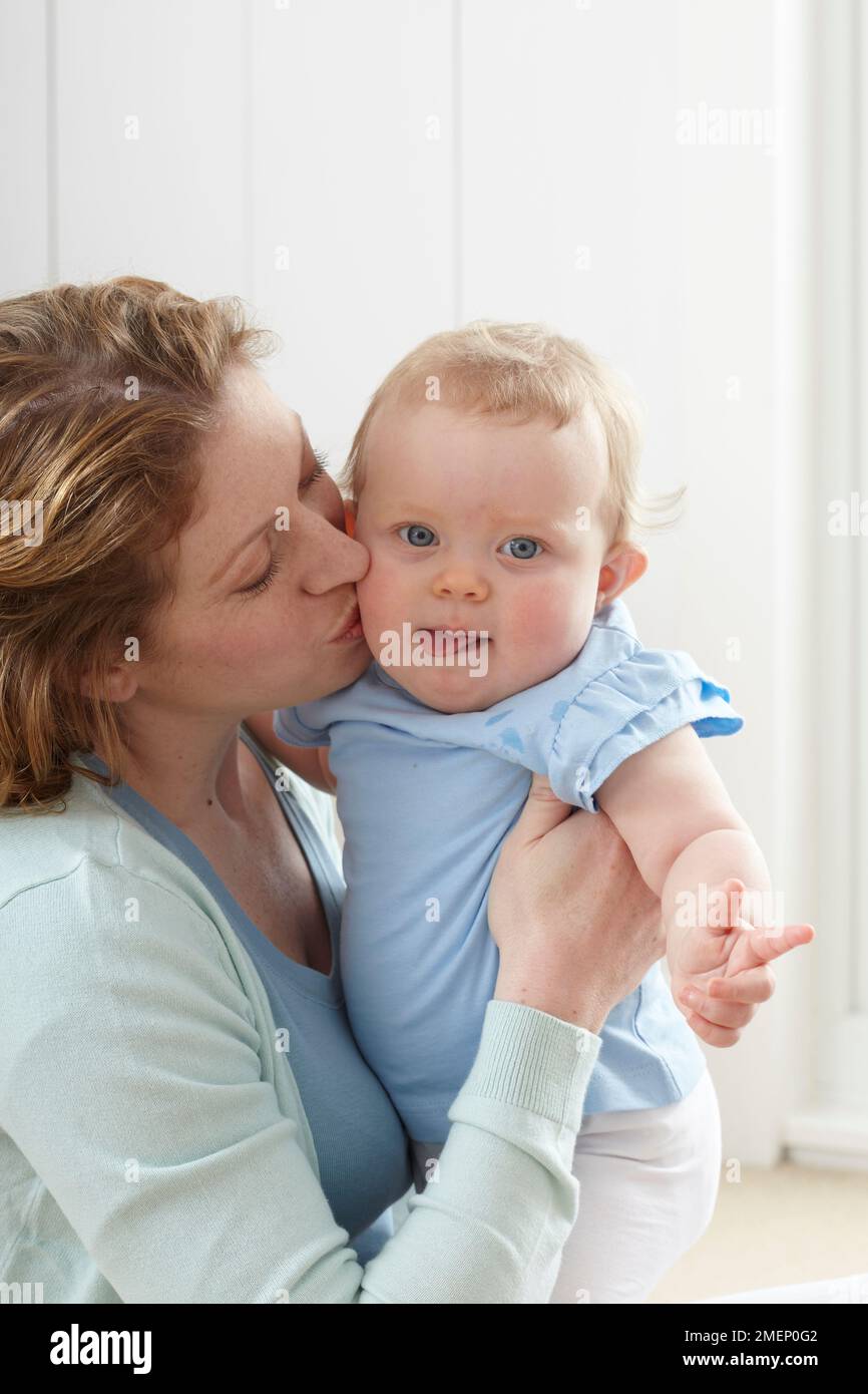 Madre seduta sulla moquette baciando la bambina (10 mesi) sulla guancia Foto Stock