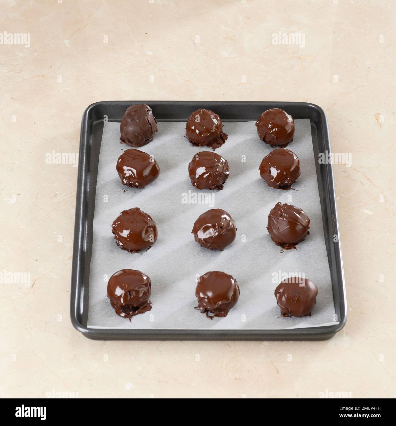 Palle di torta al cioccolato fondente, palle di torta rivestite di cioccolato disposte per asciugarsi su una teglia da forno Foto Stock