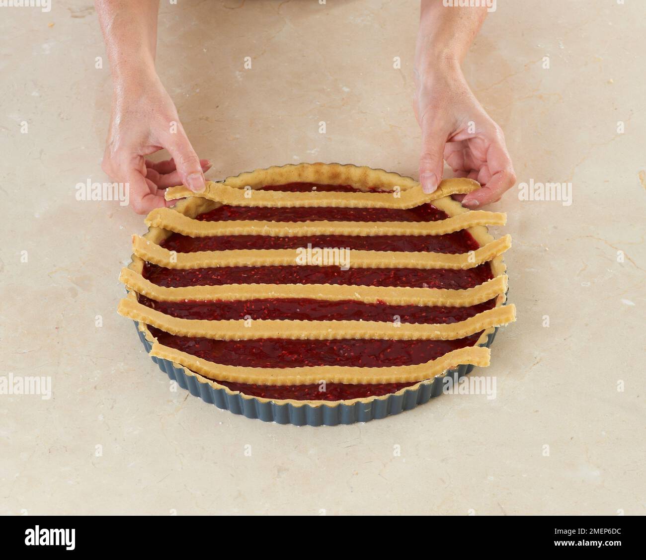 Fare la tradizionale crostata austriaca, Linzertorte, mettendo strisce di pasta sul ripieno di lamponi, per creare il reticolo modello Foto Stock