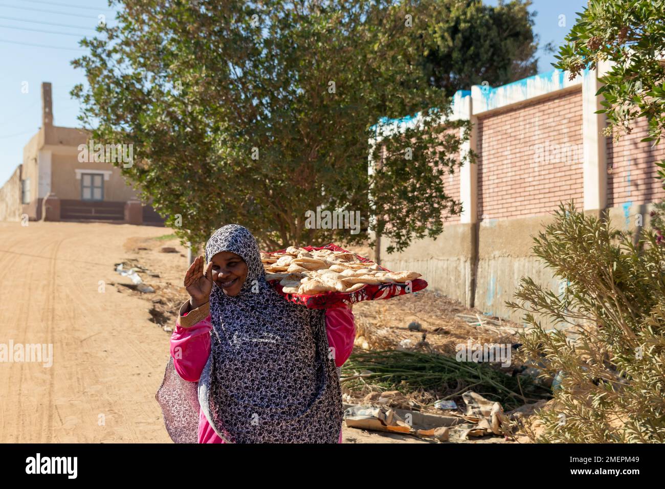 ASSUAN, EGITTO - 29 Dic 2022. Donna nubiana di mezza età, araba, musulmana con velo e abiti tradizionali con pane fresco pita fatto a mano ogni giorno scena Foto Stock