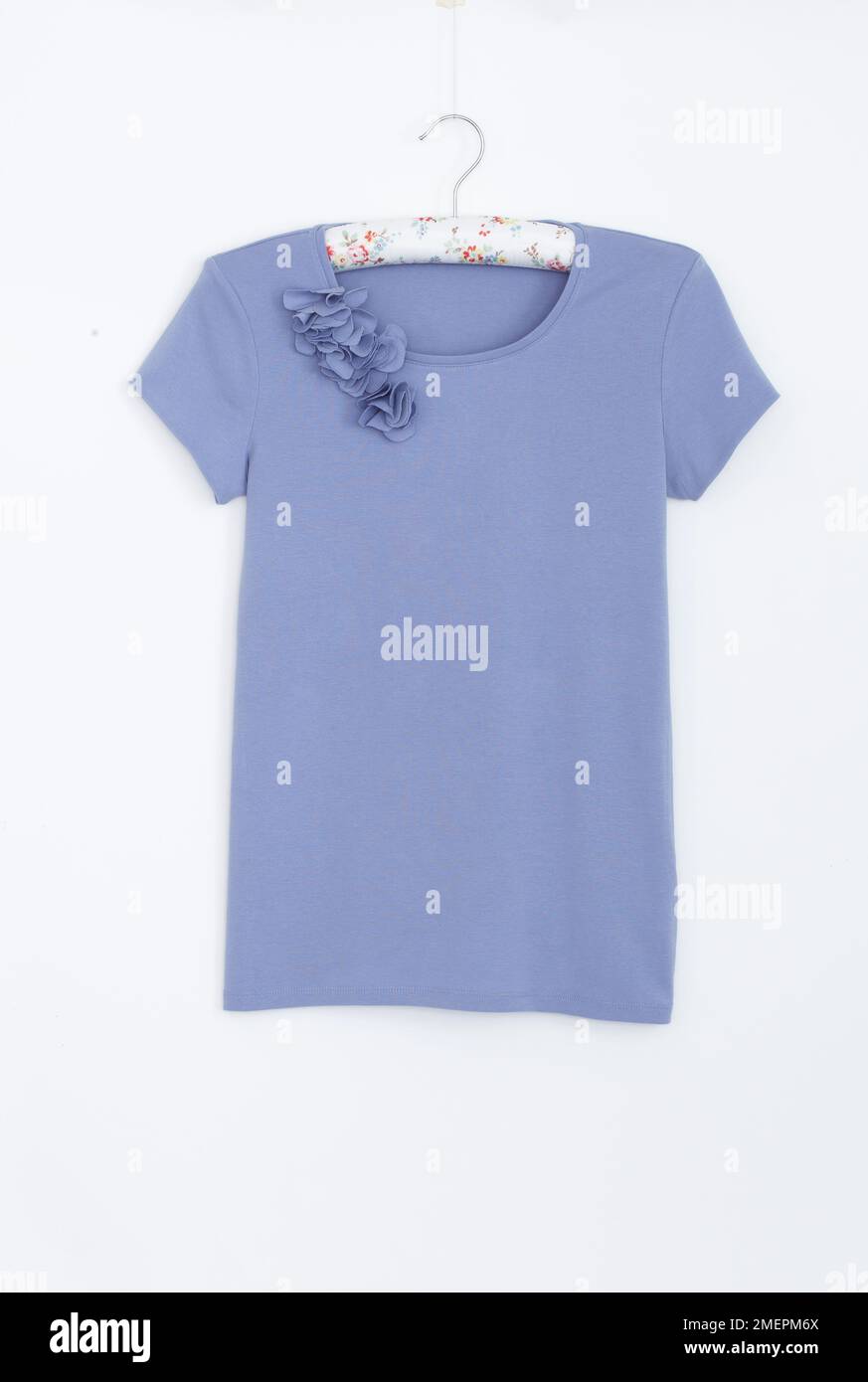 Fiori aggiunti alla scollatura della T-shirt blu, primo piano Foto Stock