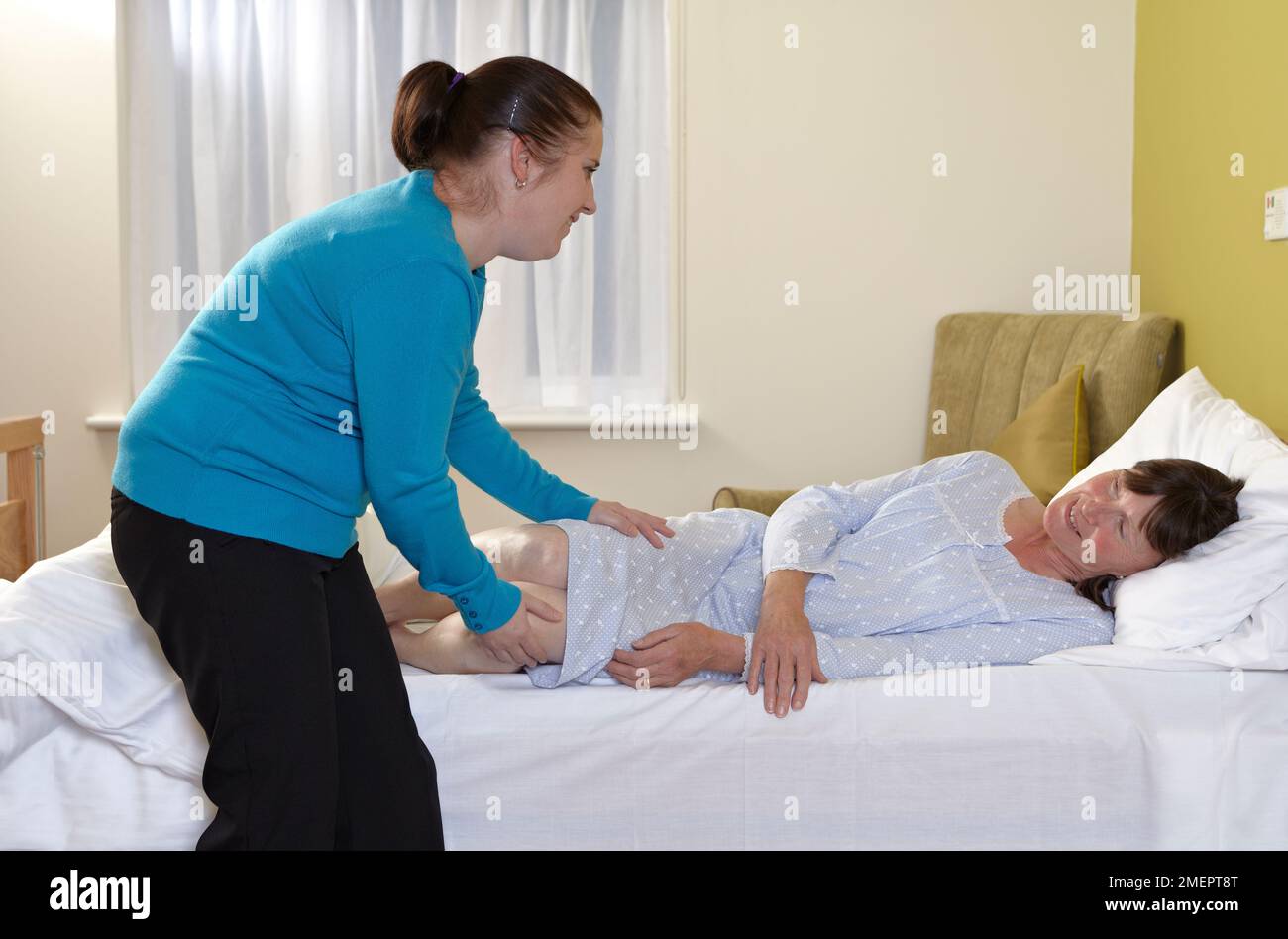 Aiutare una donna a muoversi che è sdraiata sul letto, preparandosi a sedersi Foto Stock