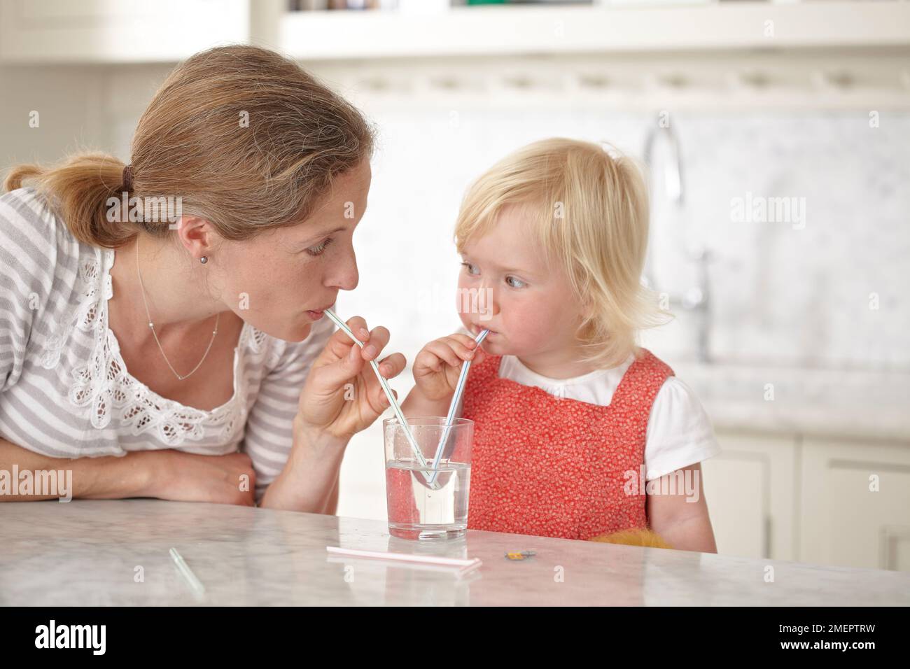 Giovane ragazza che tiene paglia in un bicchiere d'acqua, 18 mesi Foto Stock