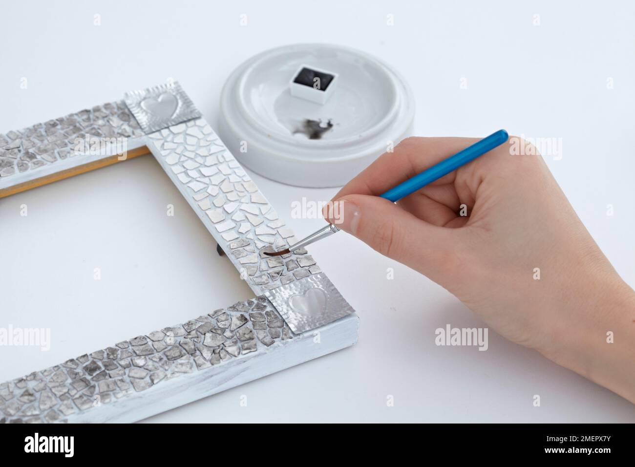 Applicazione di vernice nera e lavaggio ad acqua alla calotta del mosaico sulla cornice dell'immagine per creare un effetto chiazzato, primo piano Foto Stock