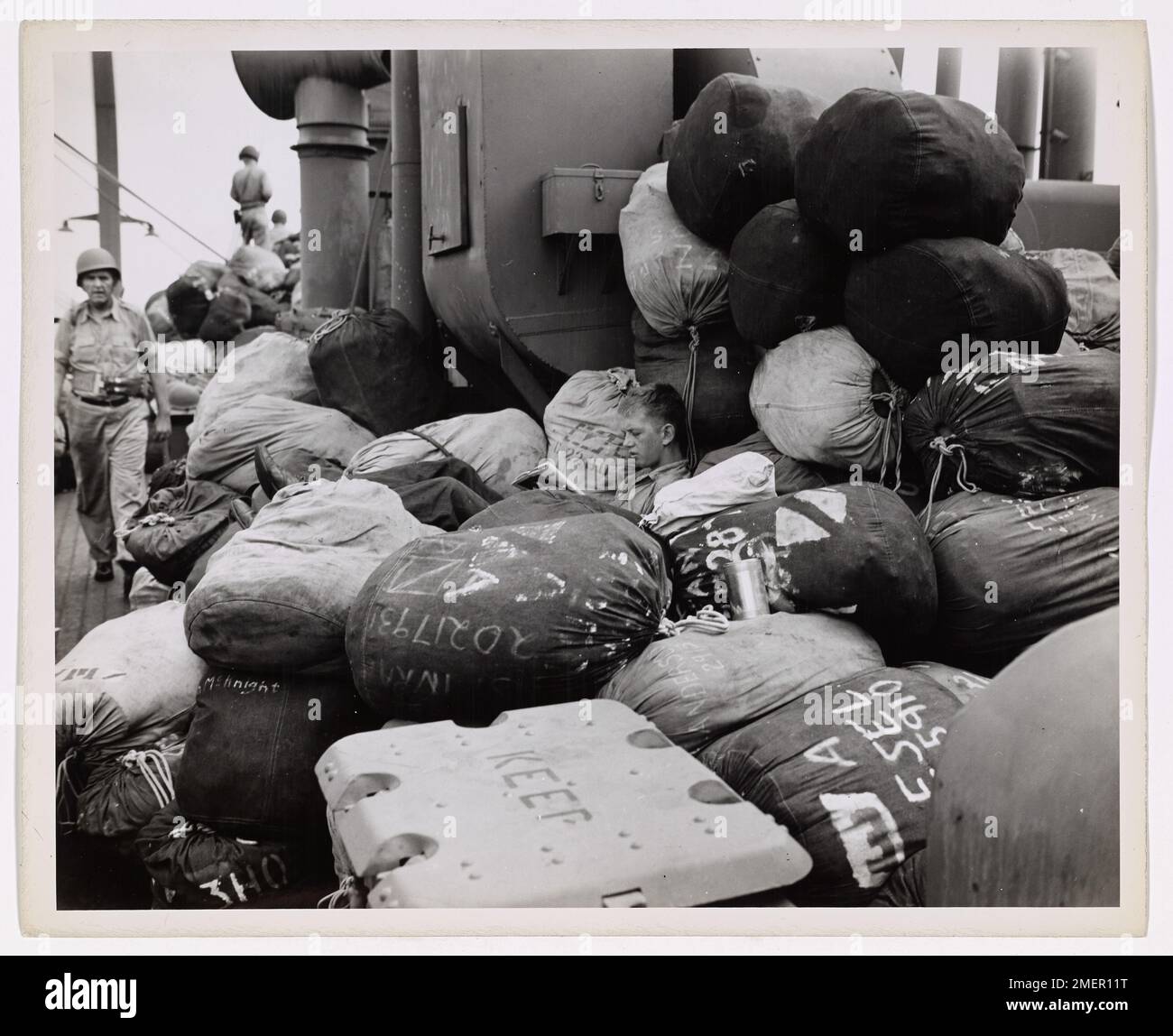 Questa immagine mostra sacchi di soldati accumulati sul ponte di un trasporto di combattimento con equipaggio della Guardia Costiera durante l'invasione di Makin. Il guardiano costiero si prende un momento per leggere mentre aspetta che i bagagli vengano scaricati. Foto Stock