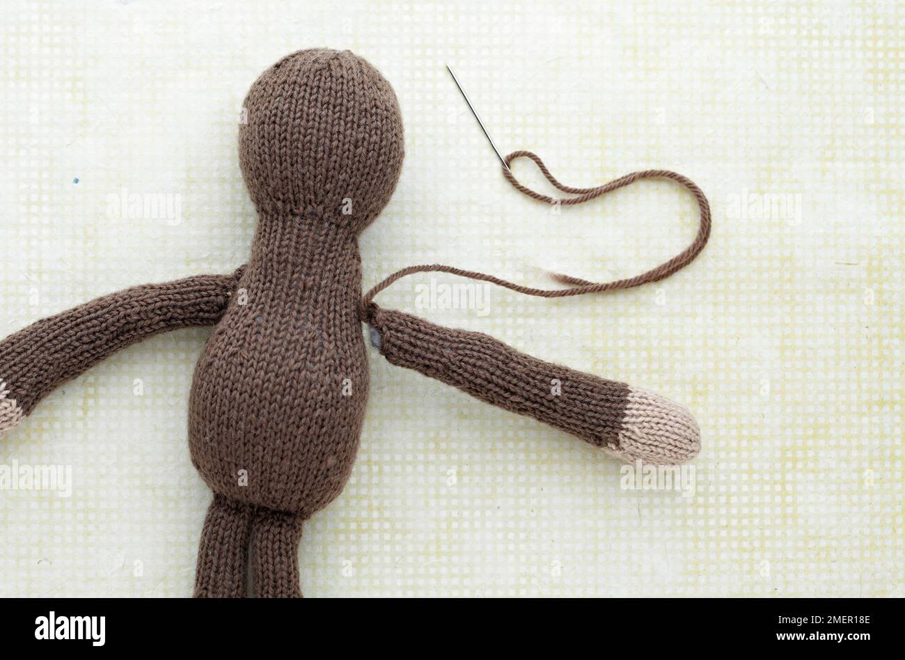 Il braccio viene cucito sulla scimmia giocattolo lavorata a maglia Foto Stock