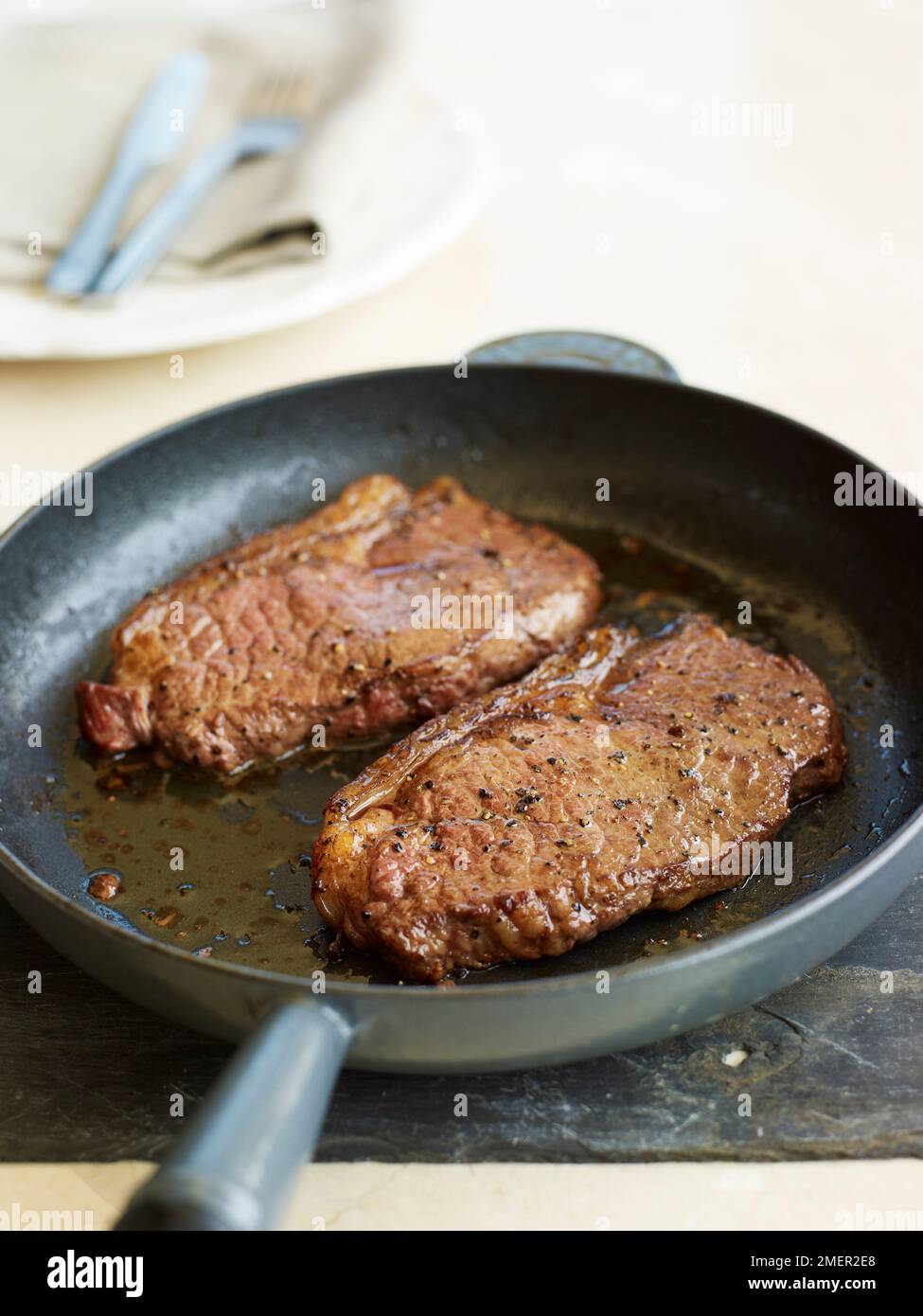 Due bistecche pepate fritte in padella Foto Stock