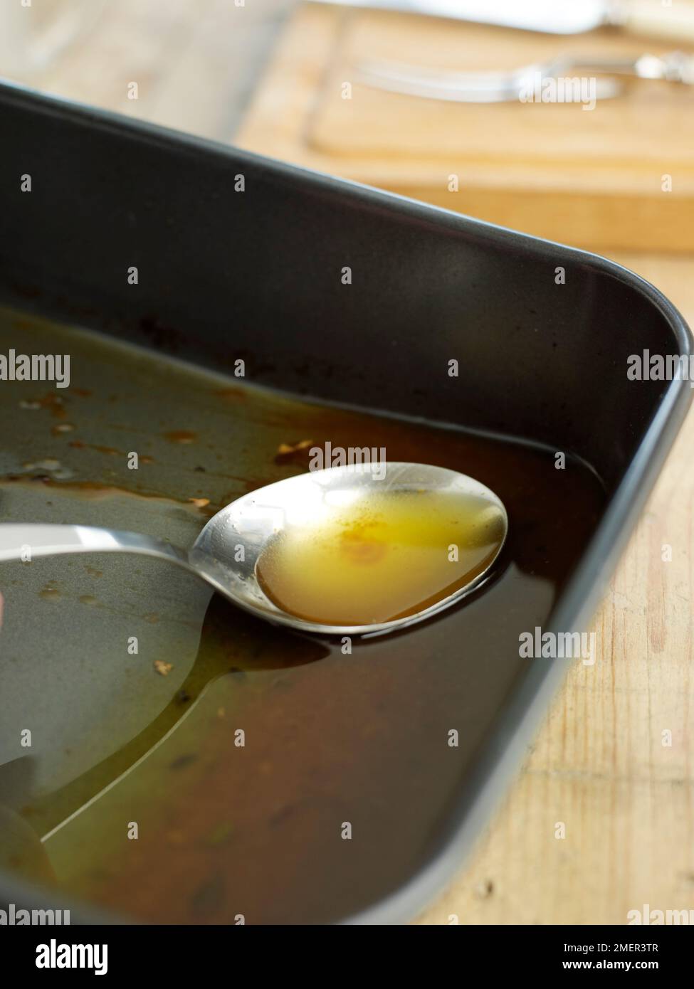 Inclinando la tostatura di stagno e di scrematura fat off inizio dei succhi di frutta, utilizzando un cucchiaio Foto Stock