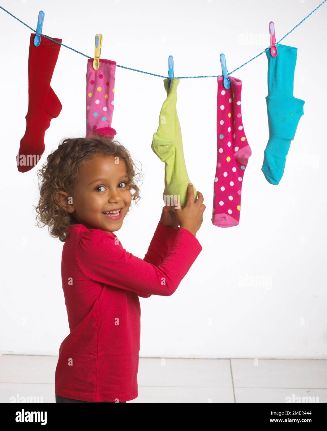 Ragazza che tiene calza in una fila di calze colorate sulla linea di lavaggio, 4 anni Foto Stock