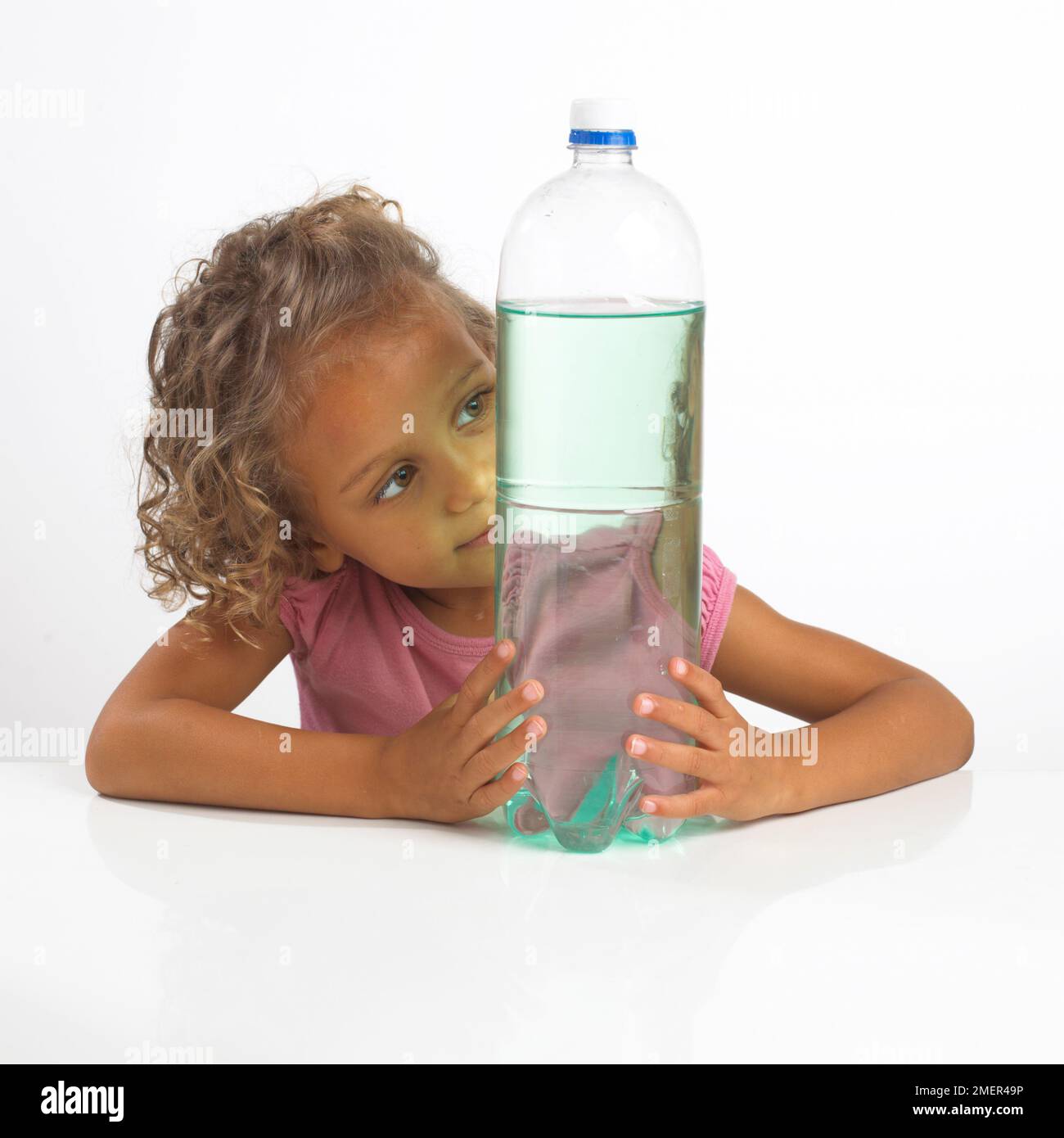 Ragazza che guarda il riflesso in una grande bottiglia d'acqua, 4 anni Foto Stock