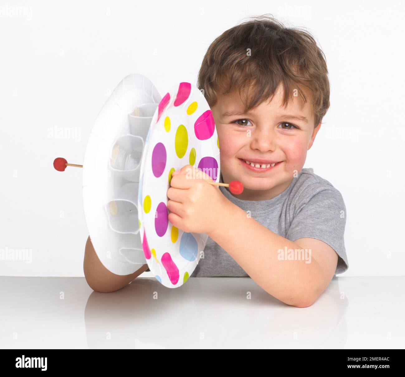 Ragazzo che indossa la parte superiore grigia che tiene la ruota dell'acqua fatta di tazze di plastica incastrate fra due piastre di carta, 4 anni Foto Stock