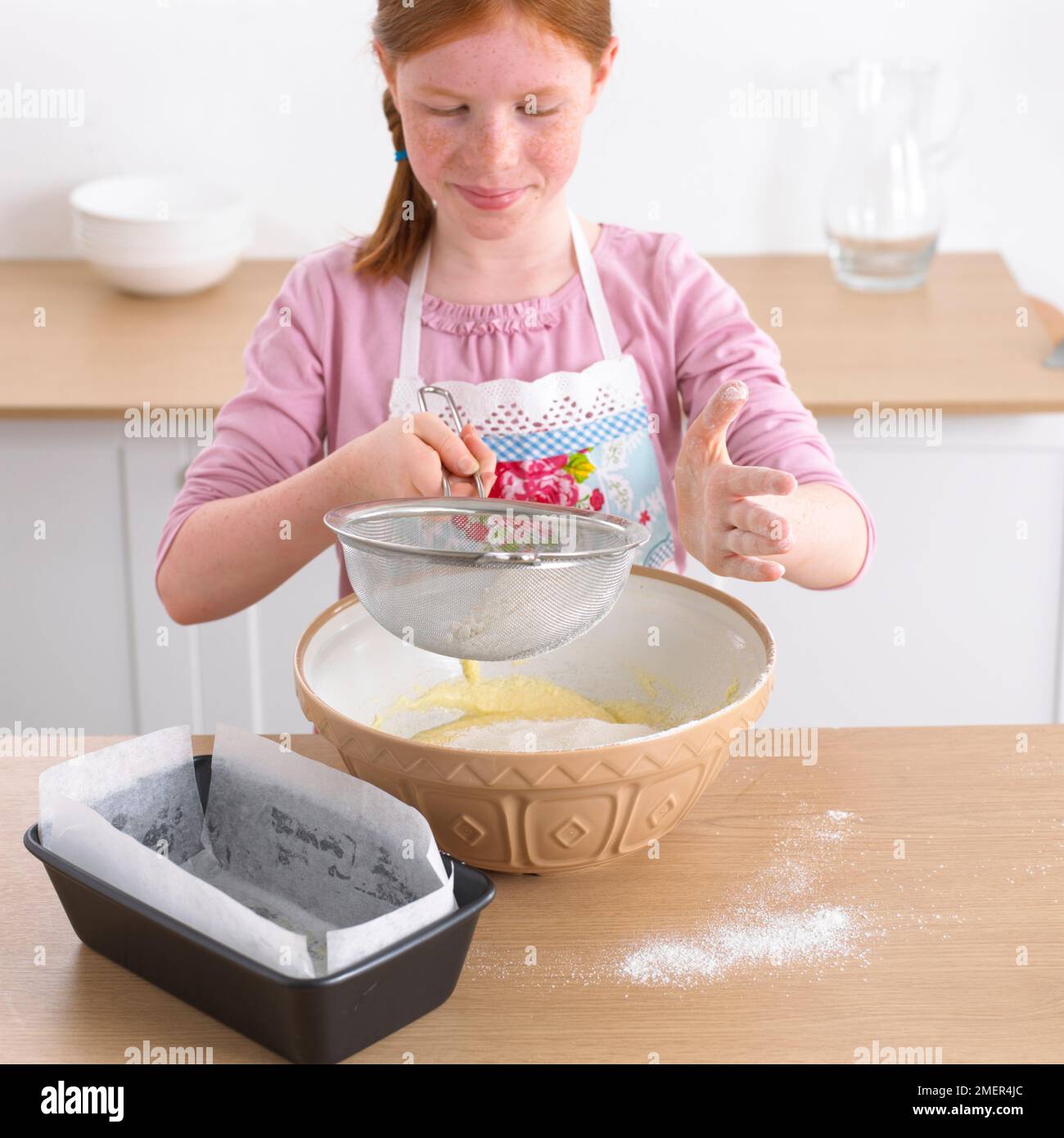 Ragazza setacciare la farina in una ciotola di impasto per torte, 9 anni Foto Stock