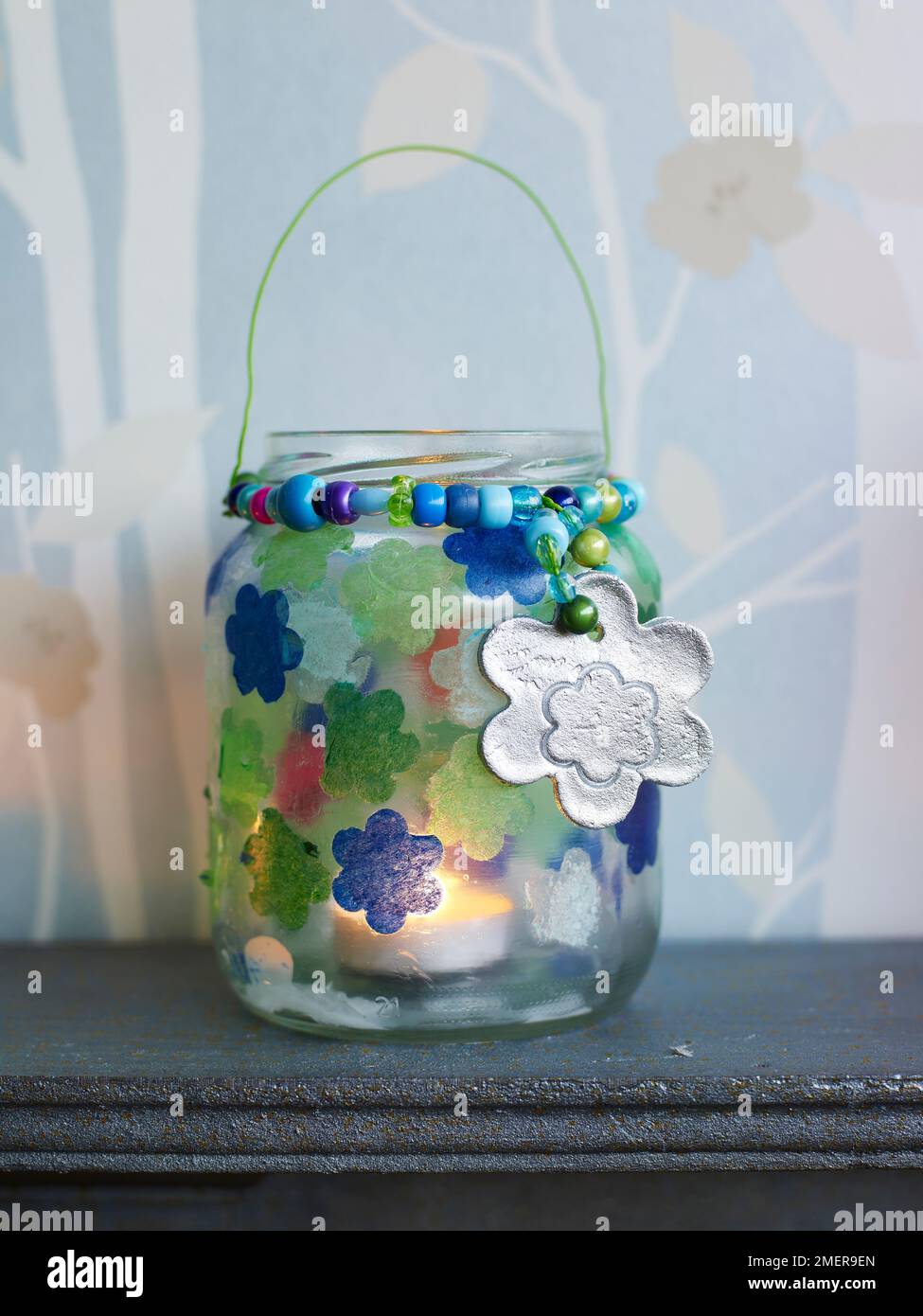 Vasi di vetro di candela decorati con fiori di carta di tessuto e pendenti d'argento, su mantelpiece Foto Stock