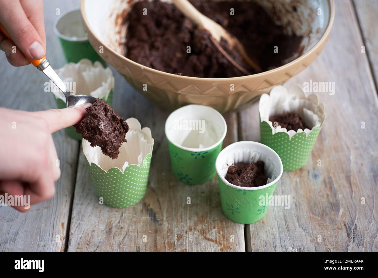 Cucchiaiare il composto della torta di cioccolato in scatole di carta, facendo le torte della flowerpot Foto Stock